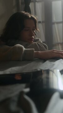 Vertical shot of bored gen Z girl doomscrolling on smartphone and checking photograph of ex-boyfriend while lying in bed at home