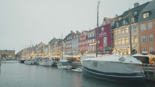 A picturesque waterfront scene featuring charming, colorful buildings lined along a peaceful canal. Boats are moored, and decorative lights create a warm ambiance, ideal for leisurely strolls and phot