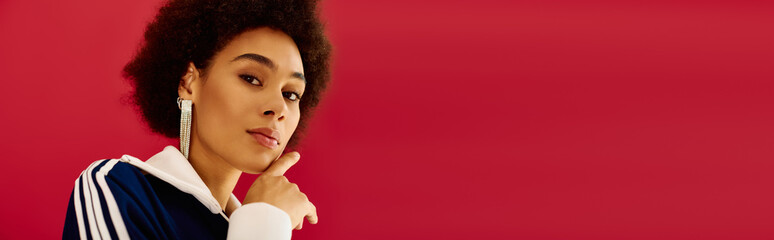 A chic and beautiful woman stands against a striking red backdrop, radiating confidence and style © LIGHTFIELD STUDIOS