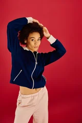 Stylish young woman poses gracefully against a vibrant red backdrop in trendy fashion outfit © LIGHTFIELD STUDIOS