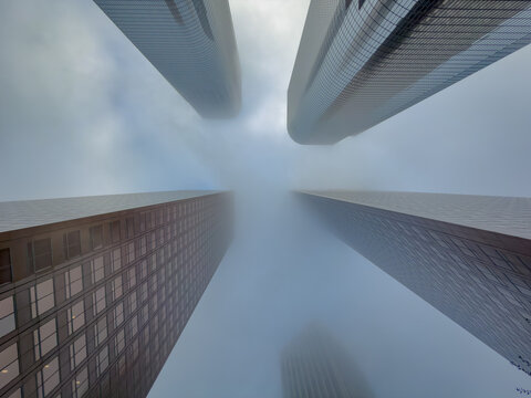 Perfect four-way symmetry looking straight up at skyscrapers, curved tops of two towers visible through swirling fog
