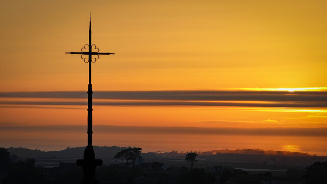 Aerial view of the silhouette of the cathedral spire against a sky ablaze with fiery hues, a symphony of light and shadow, Saint-Pol-de-Leon, Brittany, France.