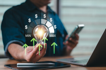 Professional businessman holding glowing lightbulb showing rising electricity costs plus dollar symbols representing financial growth plus energy efficiency dashboard near laptop computer smartphone
