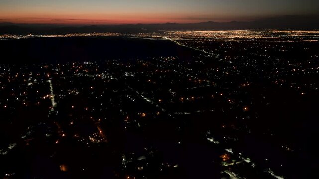 Aerial Drone View of City Lights Glowing at Dusk with mountains in the background