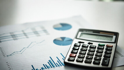 A calculator rests on charts and graphs, displaying financial data. It&rsquo;s a business scene.