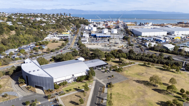 Aerial view of the distinctive curved roof of a building contrasting with the industrial port, backed by hills, Nelson, Nelson, New Zealand.