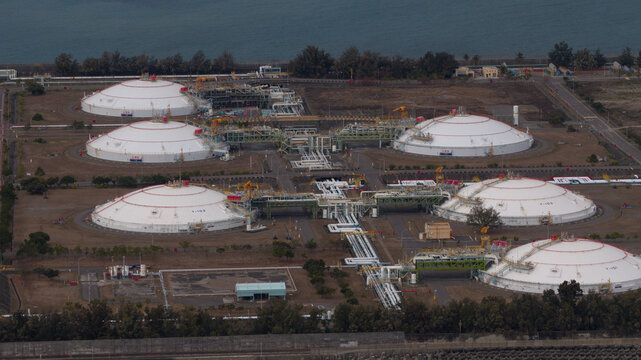 Aerial view of massive white LNG storage tanks with red tops sit neatly in a grid-like pattern, contrasting against the dark green trees, Kaohsiung City, Taiwan.