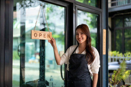 Woman smiling holding open sign at shop entrance