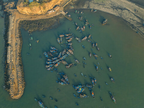 Aerial view of fishing boats bobbing in the harbor near the breakwater, a textured coastline meeting the tranquil sea, Harnai Port, Ratnagiri, Maharashtra, India.