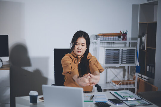 Asian female accountant is tired from working in a chair, stretching to relax and relax while working hard at the office
