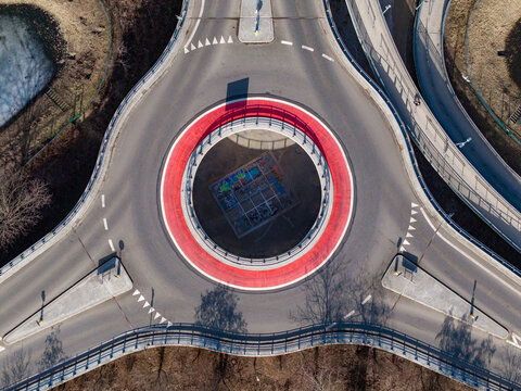 Aerial view of a vibrant red roundabout encircling a playground, framed by converging roads and the subtle textures of the urban landscape, Warsaw, Masovian Voivodeship, Poland.