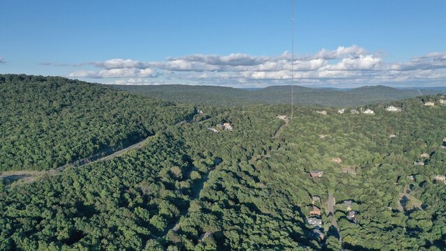 Aerial view of Monte Sano Mountain's lush canopy, dotted with homes, stretches under a vast blue sky, crowned with fluffy clouds, Huntsville, Alabama, United States.