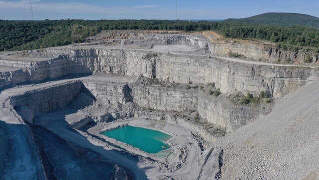 Aerial view of a deep quarry revealing layered rock formations and a turquoise pool at its base, contrasting with the surrounding greenery, Huntsville, Alabama, United States.