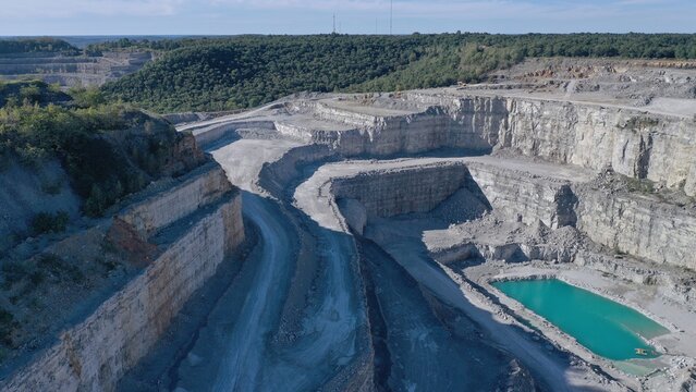 Aerial view of contrasting turquoise water nestled at the bottom of a vast quarry, surrounded by layers of grey rock and lush green trees, Huntsville, Alabama, United States.