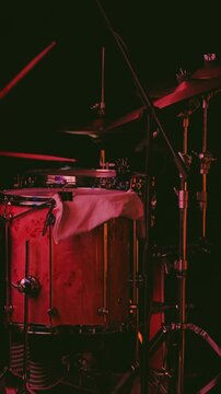 A close-up of a drummer playing on a dark stage illuminated by red concert lights. An energetic setting for a live musical performance or concert