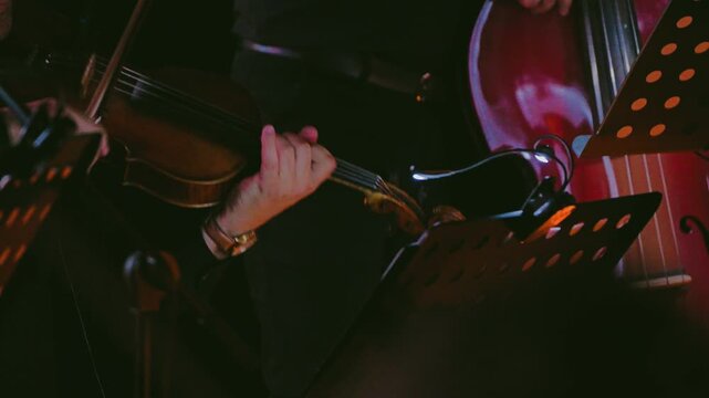 Close-up a musician's hands playing the violin at a candlelight concert. The scene is bathed in warm, dim light. Violinist performing in an orchestra during an intimate candlelight concert