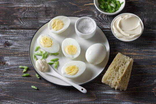 Boiled eggs with mayonnaise, green onion and bread on rustic wooden table