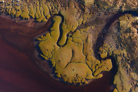 Aerial view of the rugged marshland where earthy tones meet the brown and reddish water, creating a striking contrast of textures and hues, Achnahaird, Ross and Cromarty, United Kingdom.