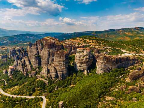 Aerial view of dramatic rock formations topped with ancient monasteries rising amidst lush greenery under a vast sky, Meteores, Trikala, Greece.
