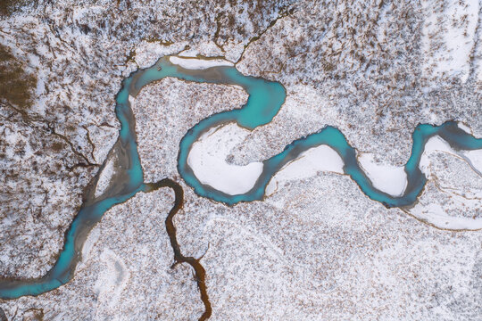 Aerial view of a turquoise river snaking through a snow-dusted landscape, creating a stunning contrast of colors and textures, Lyngen, Troms, Norway.
