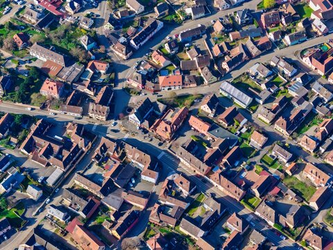 Aerial view of tightly-packed houses with red-tiled roofs interspersed with narrow streets, creating a warm patchwork of urban textures, Mittelwihr, Grand Est, France.