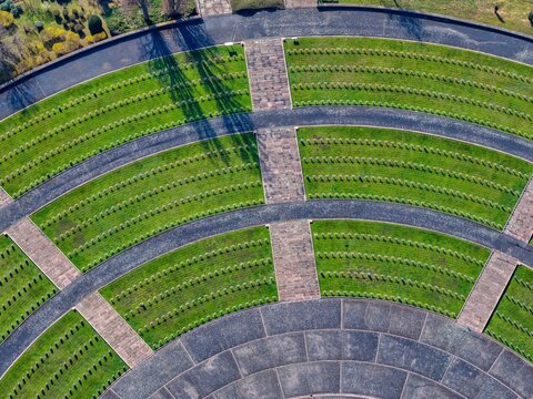 Aerial view of a circular garden with concentric green lawns and dark stone pathways creating a striking geometric pattern, Mittelwihr, Grand Est, France.