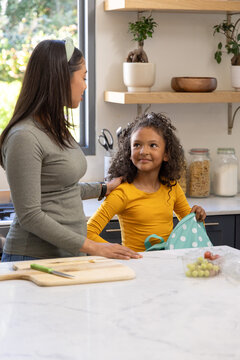 Diverse mother placing hand on child's shoulder at counter by window, child holding blue backpack