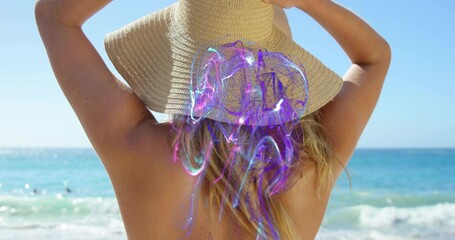 Naklejka premium Standing woman holding wide-brim straw sunhat at sandy shore, showing swimsuit and purple hologram