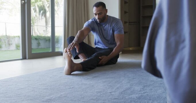 African-American man seated stretching hamstring near door reaching foot for mobility in blue tee