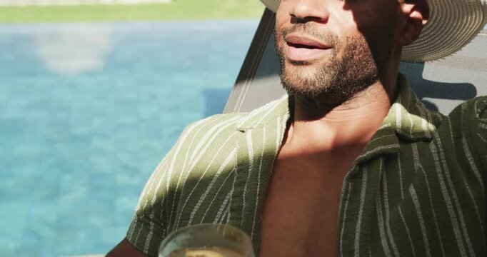 Man reacting to sunlight shifting, holding drink, adjusting white sunhat tilting head back poolside