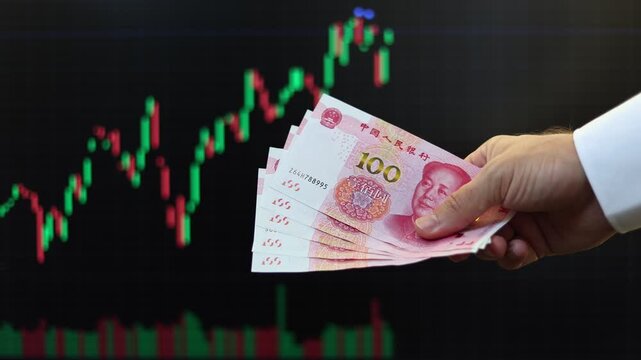 Close up view of man hands, Chinese Yuan banknotes, market chart on computer screen in background. Concept of currency growth, stock price change, volatile financial market, internet trading in China.