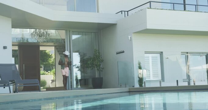 Walking man wearing white hat, shoulder bag, adjusting hat on pool deck near sliding glass doors