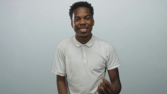 Young man in white polo shirt smiles and points two fingers at camera in a studio; confidence energy.