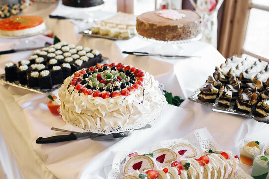 Dessert buffet table with cakes and pastries. Sweet treats arranged for guests. Fruit cake with cream and berries. Elegant dessert station for wedding reception. Catering sweets display at event.