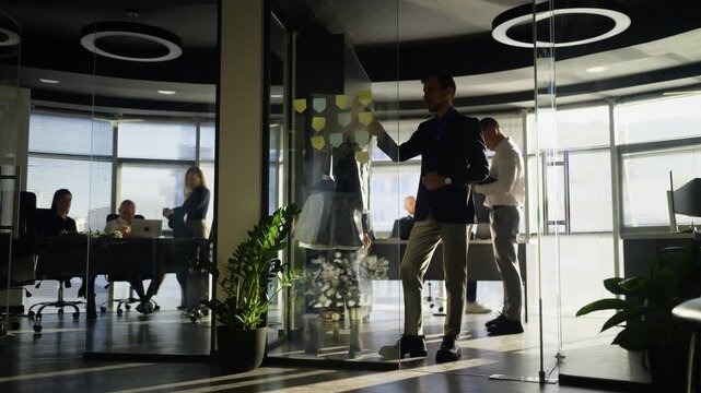 A business team collaborates, brainstorming ideas with sticky notes on a glass wall in a modern office.