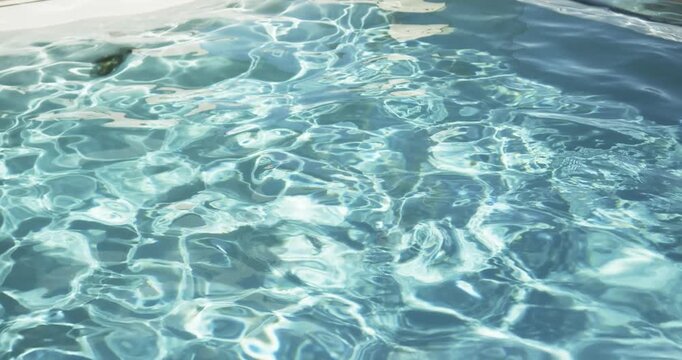 Pool water surface rippling from ripples at pool, sunlight creating shifting caustics near coping