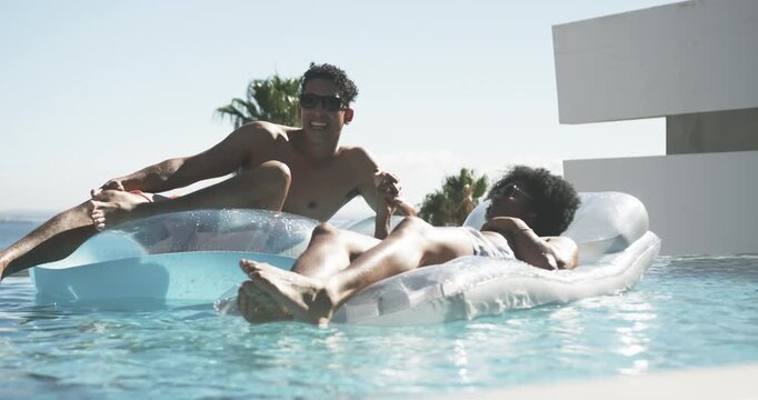 African American men on clear floats at infinity pool, man sitting up leaning holding hand laughing