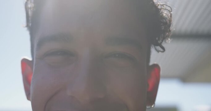 African American man smiling squinting outside from bright sun hoop earring slatted roof lens flare