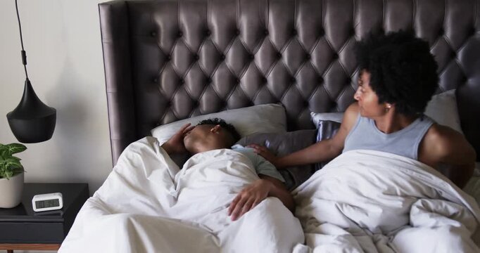 African American male pair right partner nudging sleeping partner waking him answering phone in bed