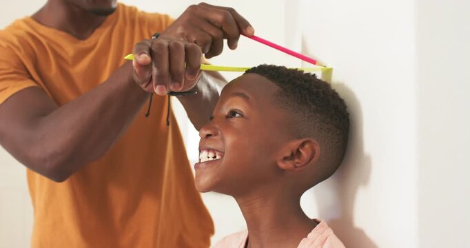 Father holding yellow tape, pink pencil, marking boy against white wall for height log, copy space