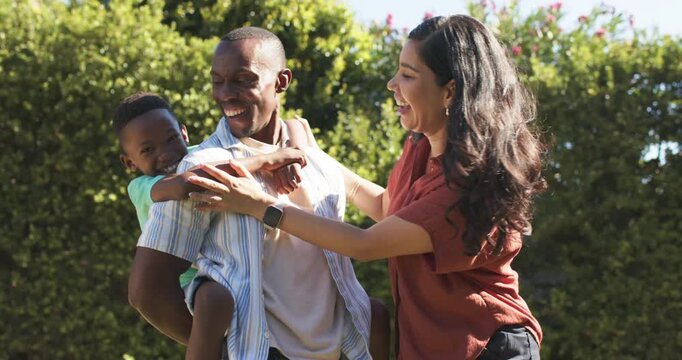 Father carrying child on back while mother approaching steadying child, posing family ad smartwatch