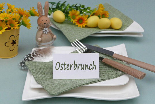 Teller mit Osterdekoration bestehend aus einem  Osterhasen bemalten Eiern, Besteck auf gr&uuml;ner Stoffserviette und einem Schild mit der Aufschrift Osterbrunch.
