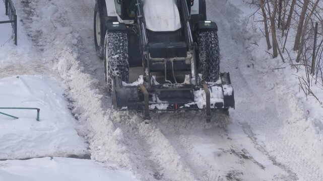 Snow removal tractor clearing deep snowdrifts from a residential driveway. High angle view of a front loader cleaning the territory after a winter storm