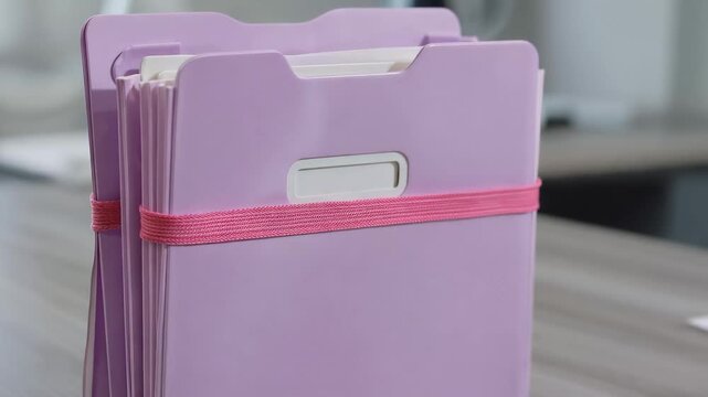Stack of Purple Folders with Pink Elastic Band on Desk Close Up Detail