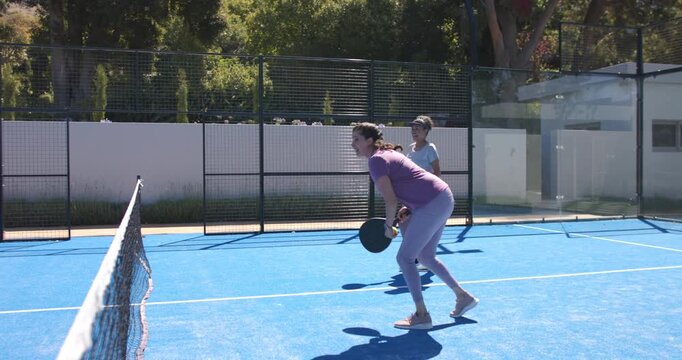 Diverse women picking near-net ball on blue court, meeting at net, shaking hands, showing goodwill