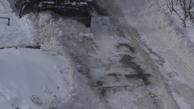 White snowplow tractor clearing a narrow residential driveway from heavy snow. Front loader machinery cleaning the local area after a snowstorm