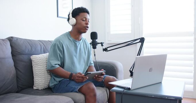 Adult African American man on sofa with headphones checking tablet singing into boom mic to record