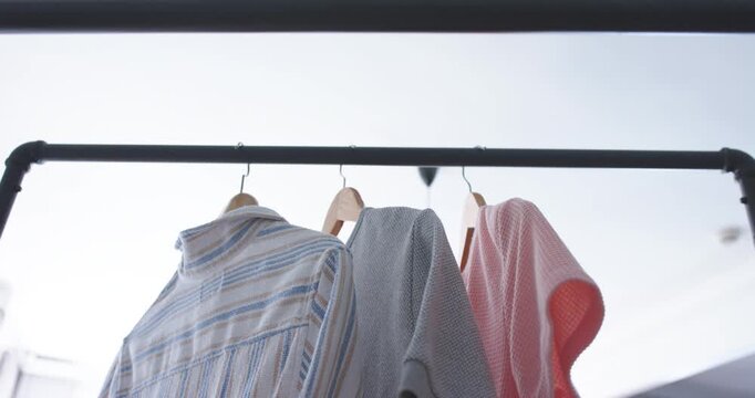 Striped shirt, gray sweater, pink knit on hangers rocking on black metal rail while camera tilting