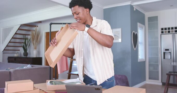 Opening shipping boxes, man unpacking and repacking at home near clothing rack with tablet