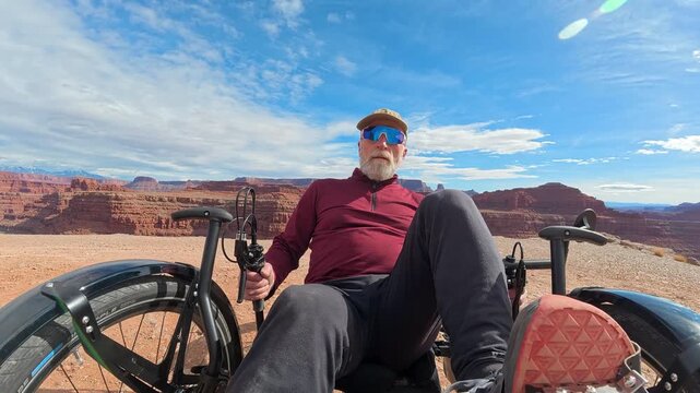 Senior cyclist is riding a full suspension recumbent tricycle off road at Thelma and Louise Point overlooking Colorado River canyon near Moab, Utah